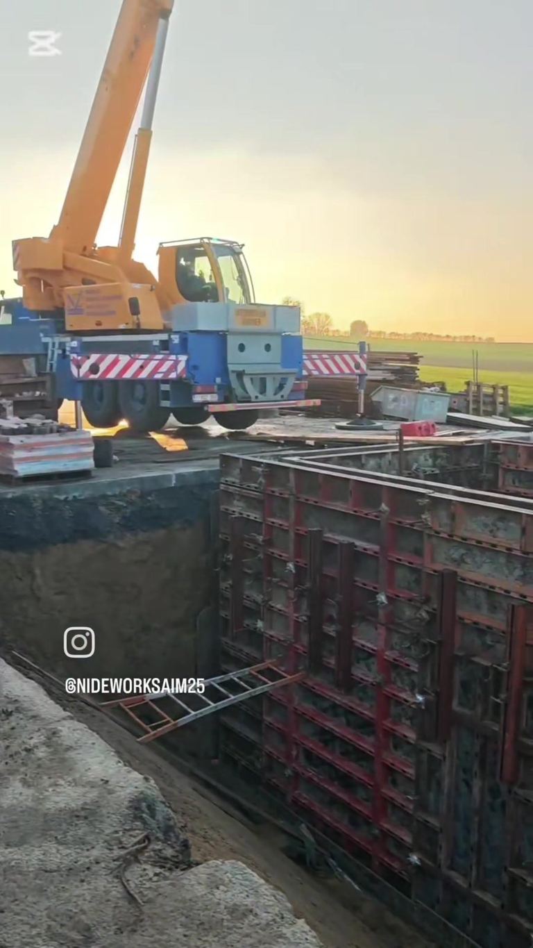 Grue mobile au-dessus de la fouille — mise en place des banches au soleil couchant
